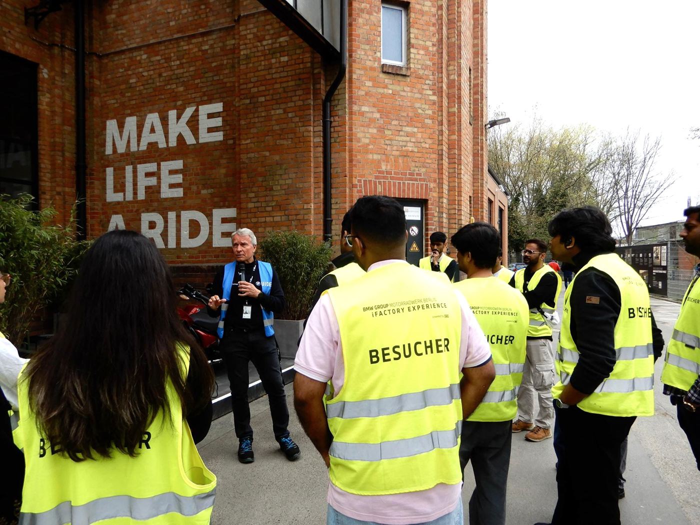 Students in visitor vests listening to a guide outside BMW Motorrad Berlin